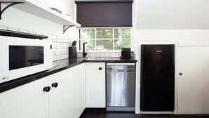 Uma cozinha moderna com armários brancos, bancada preta, micro-ondas, máquina de lavar louça e frigorífico.