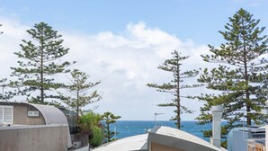 A coastal view with a clear sky, a building with a curved roof, and several pine trees. - MadeComfy Trendy Apartment on Dee Why Beach (Dee Why)