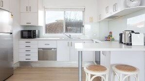 A modern kitchen with white cabinets, stainless steel appliances, a window, and a clock on the wall. - MadeComfy Trendy Apartment on Dee Why Beach (Dee Why)