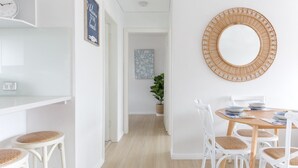 A dining area with a round wooden table, white chairs, and a woven wall hanging. - MadeComfy Trendy Apartment on Dee Why Beach (Dee Why)