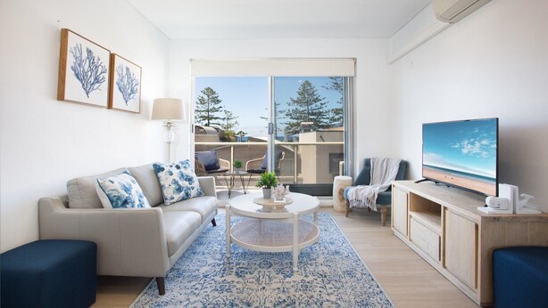 A modern living room with a sofa, coffee table, TV, and large windows. - MadeComfy Trendy Apartment on Dee Why Beach (Dee Why)