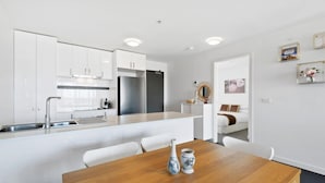 A modern kitchen with white cabinetry, a stainless steel refrigerator, and a dining area with a wooden table and white chairs. - Executive and Spacious Apartment with Balcony (Sunshine)