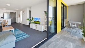 A modern living room with a flat-screen TV, a sofa, a dining table, and a glass door leading to a balcony. - Executive and Spacious Apartment with Balcony (Sunshine)