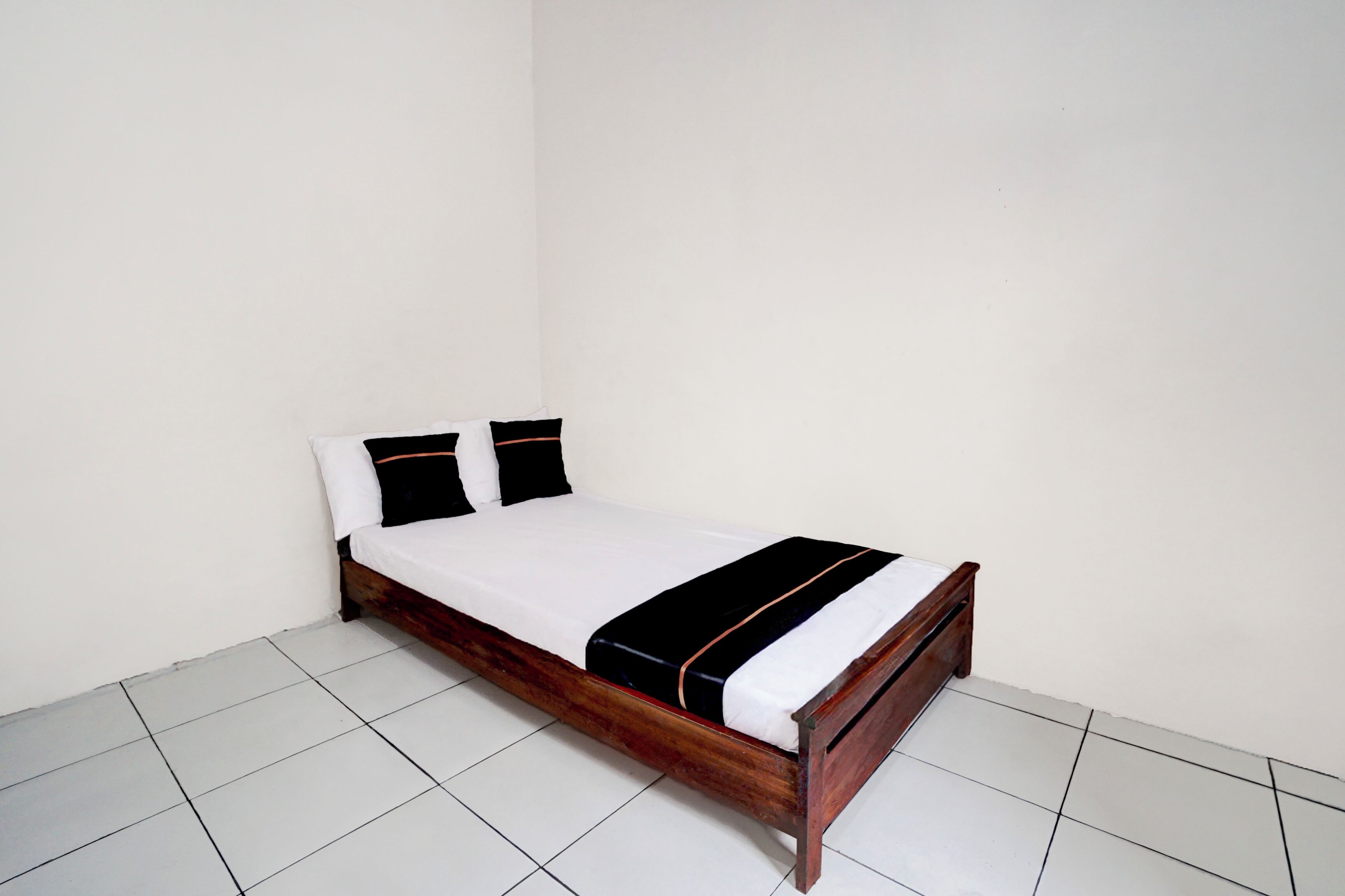 A single bed with a wooden frame, white bedding, and a black and white striped blanket.