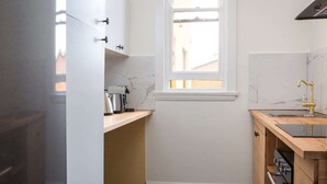A compact kitchen with white cabinets, a marble backsplash, a window, and a wooden countertop. - Central 2-Bed Apartment with Private Parking (Strathfield)