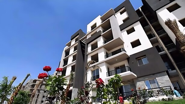 A multi-story residential building with balconies, a clear sky, and some greenery. - Elegant Apartment at Sheikh Zayed Compound (Sheikh Zayed)