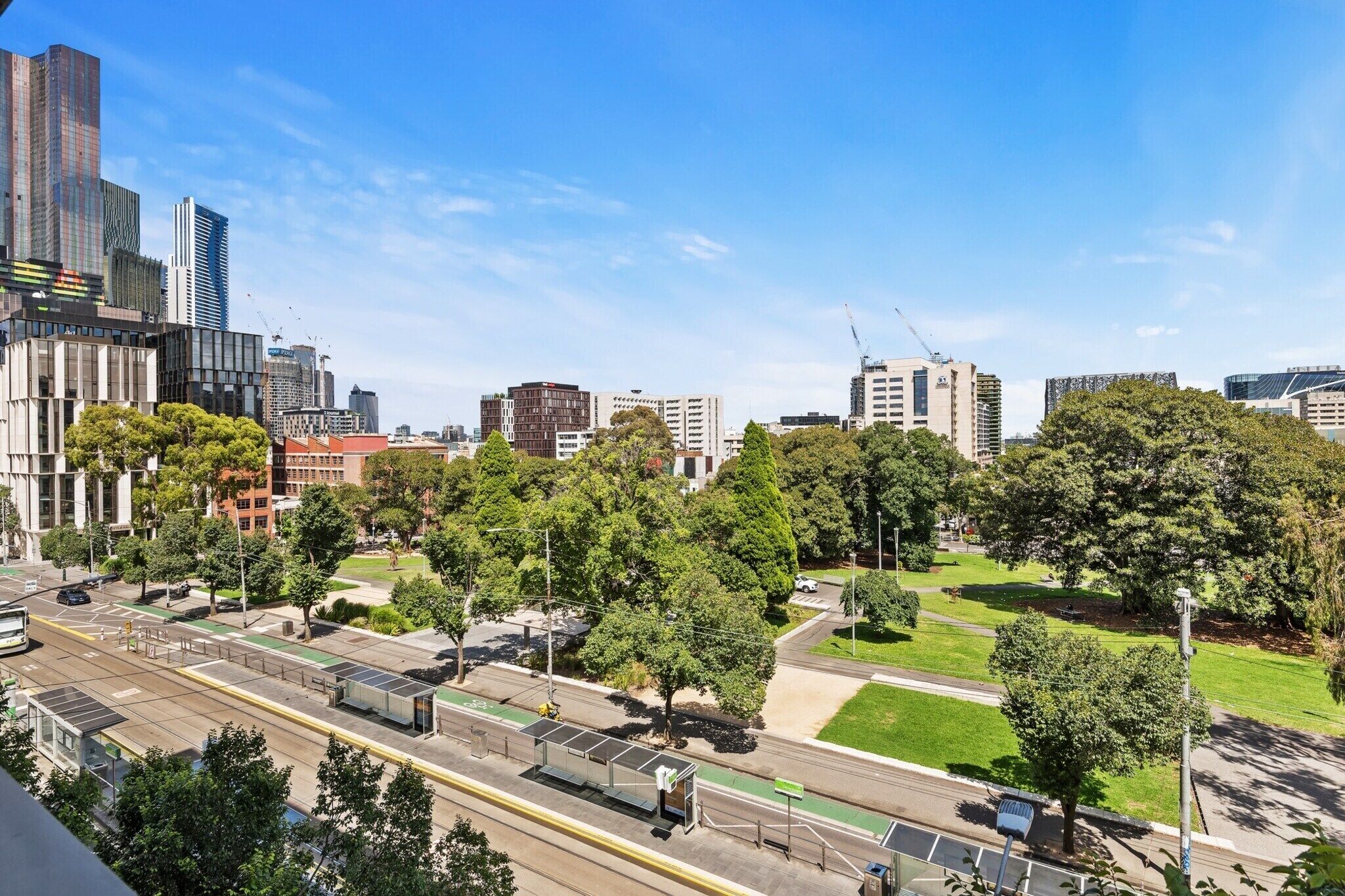 Un paysage urbain avec des bâtiments modernes, un espace vert aménagé en parc et une ligne de tramway.