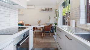 Une cuisine moderne avec des meubles blancs, un four encastré et un coin repas comprenant une table et des chaises.