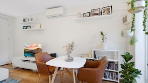 Un salon moderne avec un téléviseur blanc, deux fauteuils marron, une table blanche et une bibliothèque.