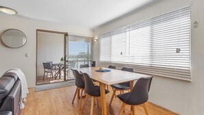 Un comedor moderno con una mesa de madera y sillas negras, un espejo redondo en la pared y un puerta corrediza de vidrio que da a un espacio exterior.
