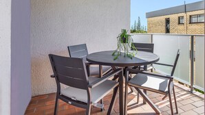 Un patio con una mesa redonda y cuatro sillas, una planta en maceta y una vista de un edificio al fondo.