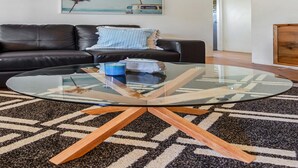 Una sala de estar con una mesa de centro de vidrio, un sofá de cuero negro y un tapete estampado.
