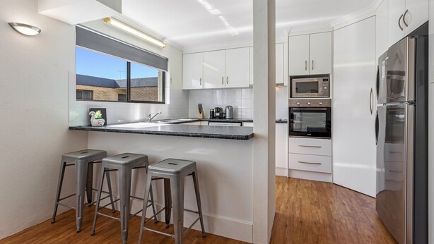 Una cocina moderna con armarios blancos, electrodomésticos de acero inoxidable y una zona de bar con taburetes.