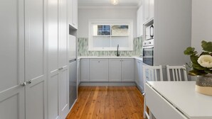 Una cocina estrecha con armarios blancos, piso de madera y ventana con vistas.