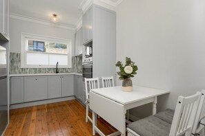 A kitchen with white cabinets, a white table, and a window. - Coastal Living Just Metres From Coogee Beach (Coogee)