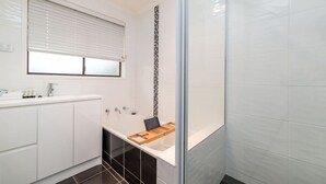 A modern bathroom with a bathtub, a shower, and a vanity with a mirror. - Spacious and Restful Holiday Home with Backyard (Cook)