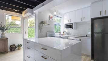 A modern kitchen with white cabinetry, a central island, a built-in microwave, and a stainless steel refrigerator.