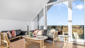 A spacious living area with a large sliding glass door leading to a balcony, a black leather sofa, a wooden coffee table, and a small round table. - "Saxi" - 650m from the sea by Interhome (Skagen)