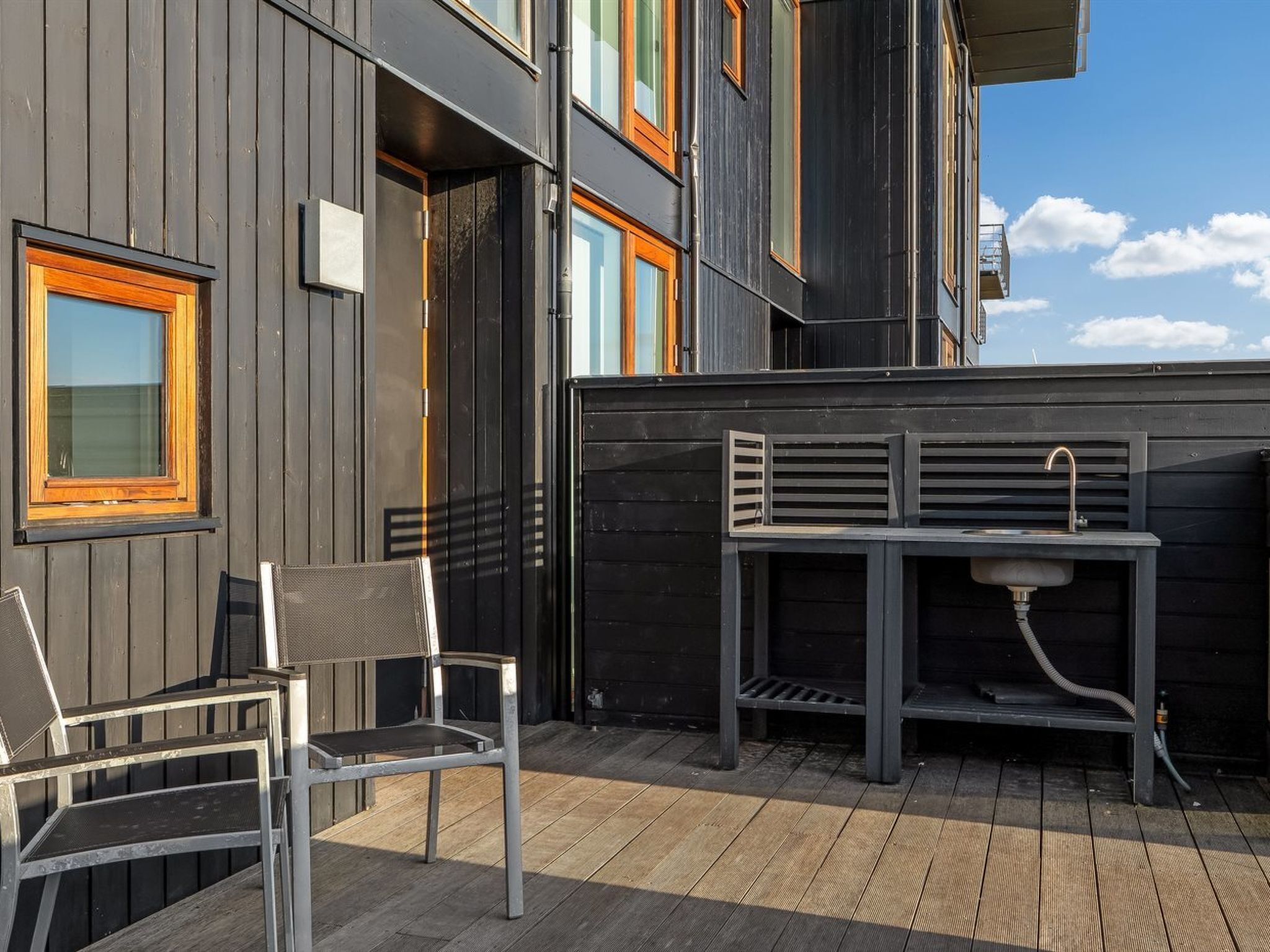 A modern outdoor seating area with a metal table and chairs, a built-in sink, and a wooden deck.