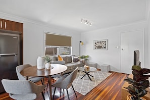 A modern living room with a dining area, a gray sofa, a coffee table, and a large window with blinds. - Windsor Cosy 2-Bedroom Unit in Quiet Neighborhood (Windsor)