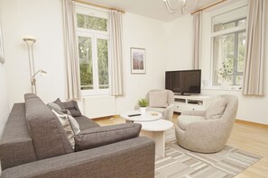 A modern living room with a sofa, armchairs, a coffee table, and a TV. - Villa Odin - Beautiful 2-room apartment with a veranda - Villa Odin FeWo Ostseerauschen (Sellin)