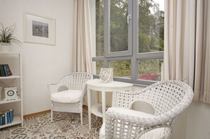 A room with two wicker chairs, a small round table, a bookshelf, and a window with curtains. - Villa Odin - Beautiful 2-room apartment with a veranda - Villa Odin FeWo Ostseerauschen (Sellin)