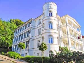 A multi-story building with a rounded tower, large windows, and a balcony on the upper floor. - Villa Odin - Beautiful 2-room apartment with a veranda - Villa Odin FeWo Ostseerauschen (Sellin)