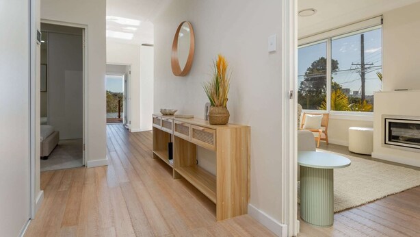 A modern living room with a fireplace, a large window, and a wooden console table with decorative items. - Idyllic 4-Bed Home With Alfresco Area Near Beach (Dee Why)