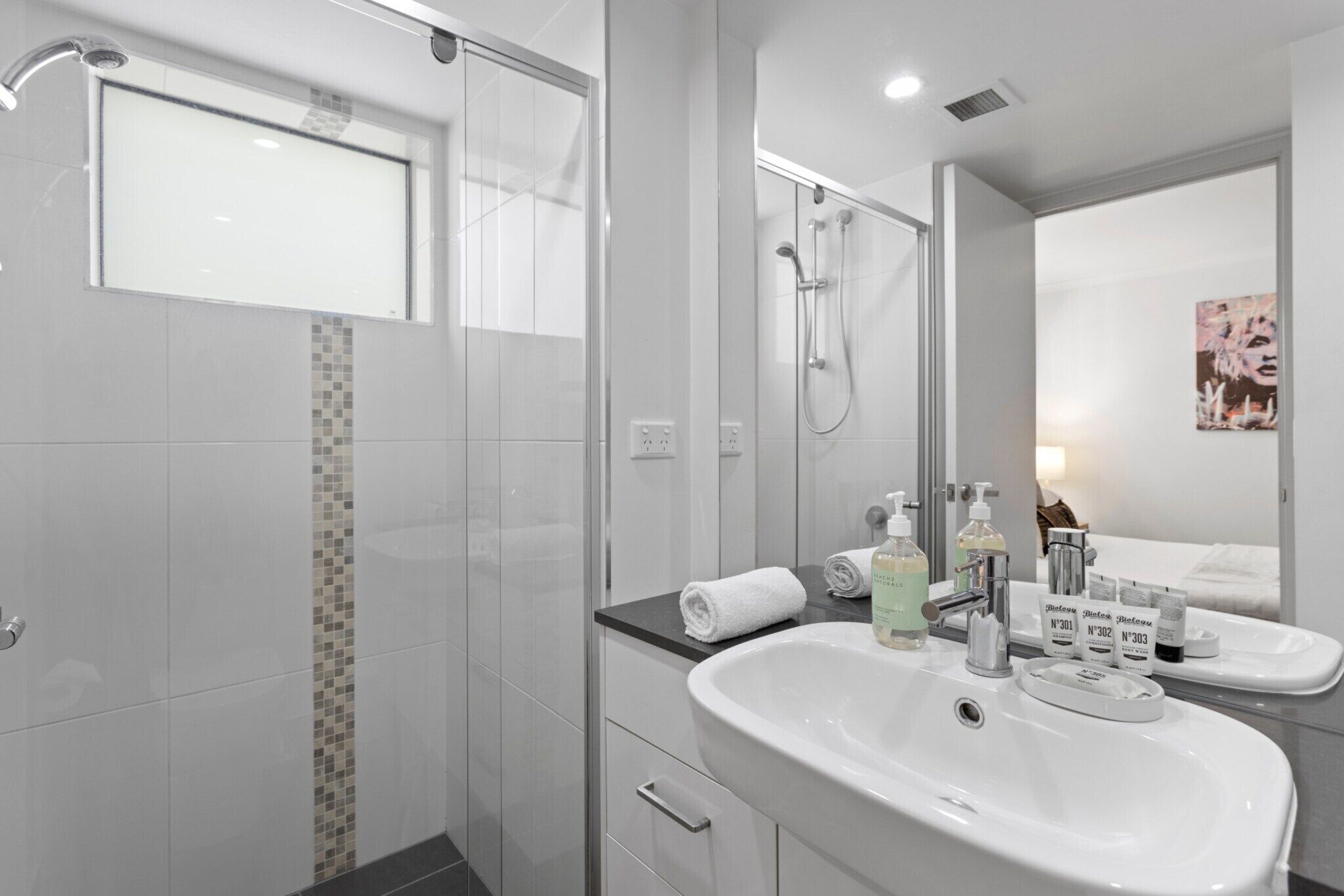 A modern bathroom with a glass shower enclosure, a large mirror, and a white sink with toiletries.