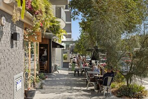 Een terras met tafels en stoelen, planten in potten, en een gebouw met nummerborden.