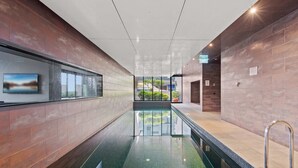 A modern indoor pool area with a glass wall, a view of greenery outside, and an exit sign. - Modern 1-Bed City Apartment with Pool and Gym (Melbourne)
