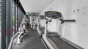 A gym with treadmills, ellipticals, and weight machines, with large windows offering views of the outside. - Modern 1-Bed City Apartment with Pool and Gym (Melbourne)