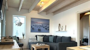 Uma sala de estar moderna com um sofá cinzento, mesa de centro de madeira e uma pintura com uma cena de praia.