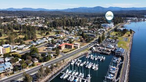 An aerial view of a coastal town with a marina, residential areas, and a prominent building with a red roof. - Elegant 2-Bed Apartment with Incredible Bay Views (Batemans Bay)