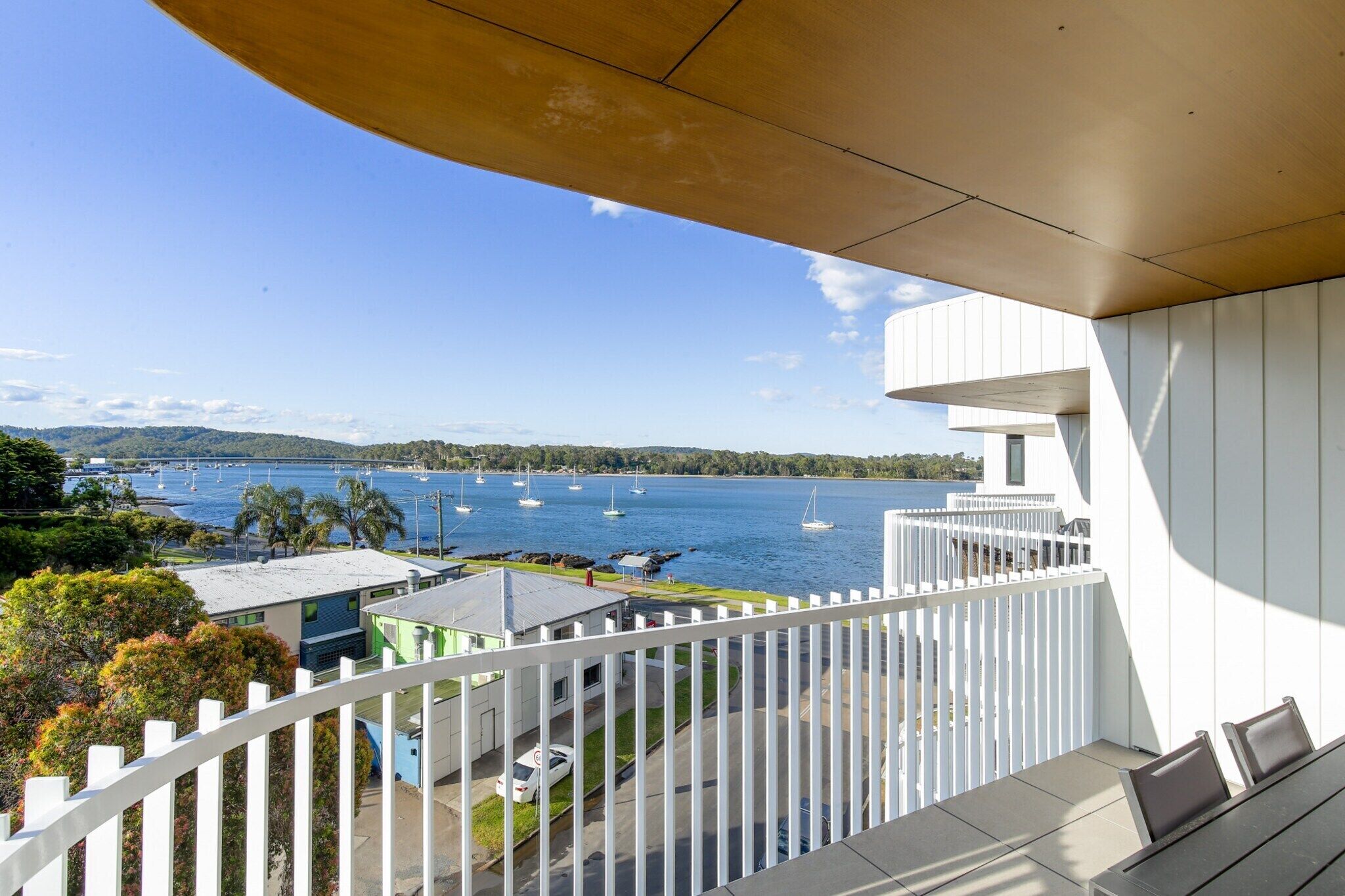 A balcony with a view of a lake and boats, white railings, and a building in the background.