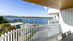 A balcony with a view of a lake and boats, white railings, and a building in the background. - Bay View 2-Bedroom Apartment with BBQ (Batemans Bay)