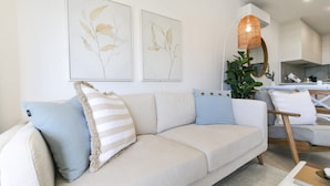 A modern living room with a beige sofa, striped pillows, and two wall-mounted plant prints. - Bay View 2-Bedroom Apartment with BBQ (Batemans Bay)