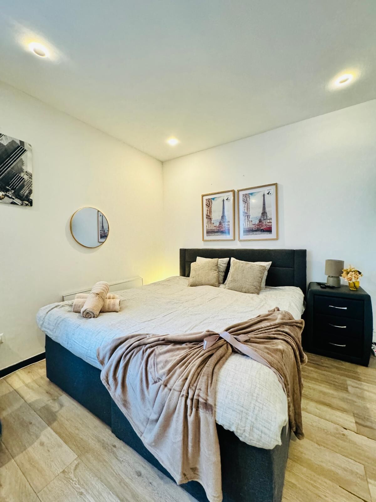 Une chambre à coucher moderne avec un grand lit, une table de chevet avec une lampe et deux tableaux encadrés accrochés au mur.