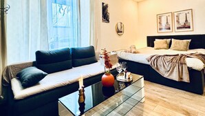 Een moderne woonkamer met een bank, een glazen salontafel en een bed met hoofdeinde.