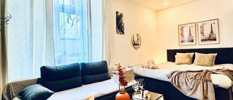 A modern living room with a sofa, a glass coffee table, and a bed with a headboard.