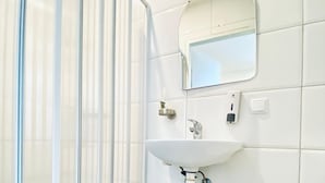 Een badkamer met een douchecabine van glas, een wastafel met spiegel erboven en een toilet.