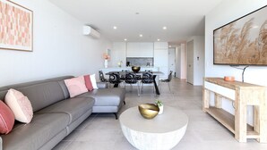 Uma sala de estar moderna com um sofá cinzento, uma mesa de centro redonda e uma área de refeições com uma mesa e cadeiras em preto e branco.