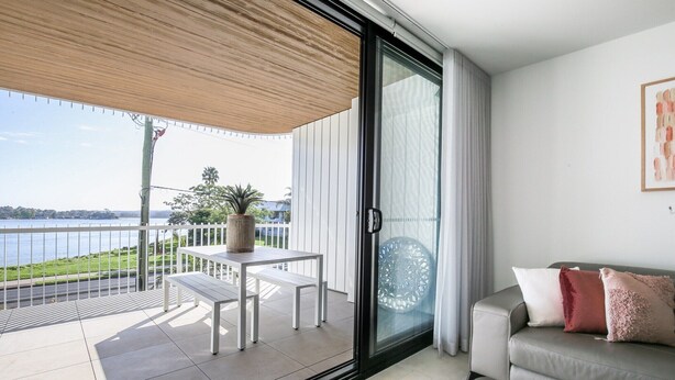 Varanda com mesa, banco, porta de vidro deslizante e sofá cinza com almofadas.