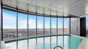 Ein moderner, überdachter Pool mit Blick auf die Stadt, großen Fenstern und blauem Himmel.