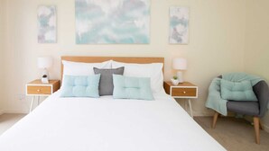 Un dormitorio ordenado con una cama grande, dos mesitas de noche y una silla.