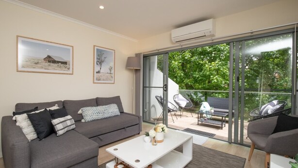 Una sala moderna con un sofá gris, una mesa de centro blanca y un balcón con mobiliario exterior.