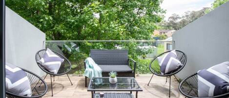 A balcony with wicker furniture, a glass table, and a potted plant.