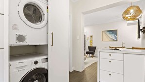 A modern laundry room with a Samsung washing machine, a white cabinet with drawers, and a large window. - Comfy 2-Bed Apartment with A/C throughout (Manly)