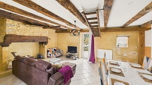 Un soggiorno rustico con travi a vista in legno, un divano in pelle, una televisione e un'area pranzo con tavolo imbandito per quattro persone.