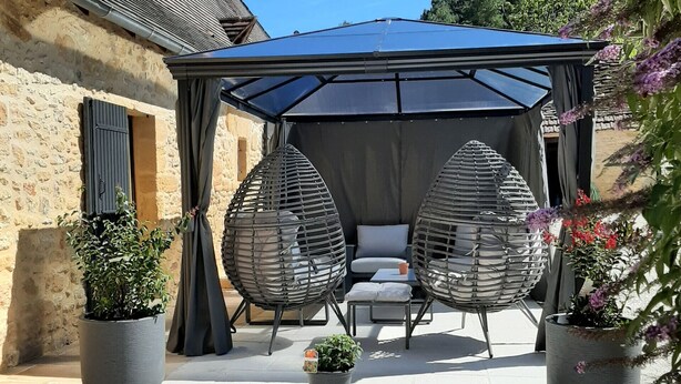 Un'area patio con due poltrone in vimini, un tavolino e una zona salotto coperta.